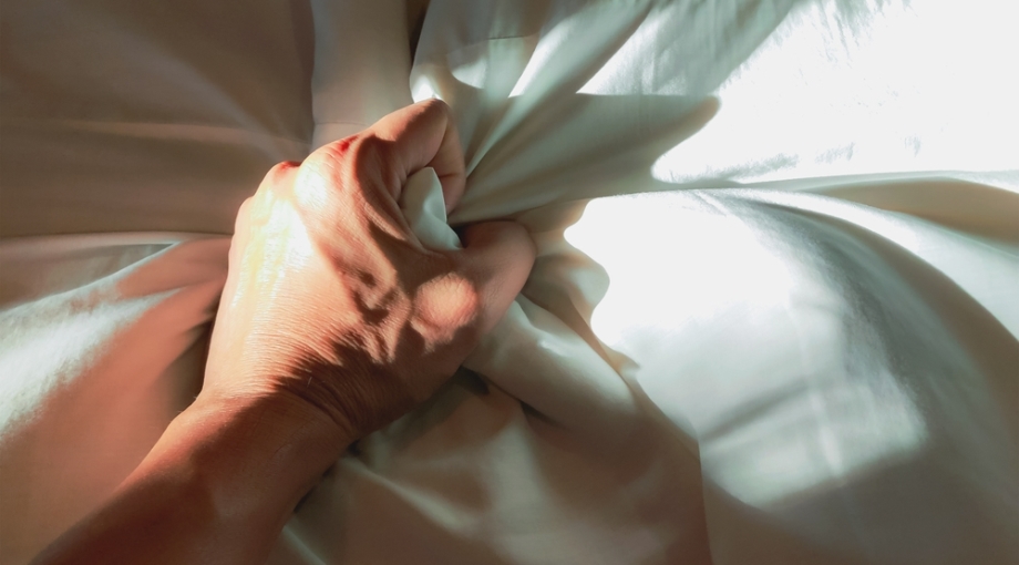 Man's hand pulling sheet during orgasm